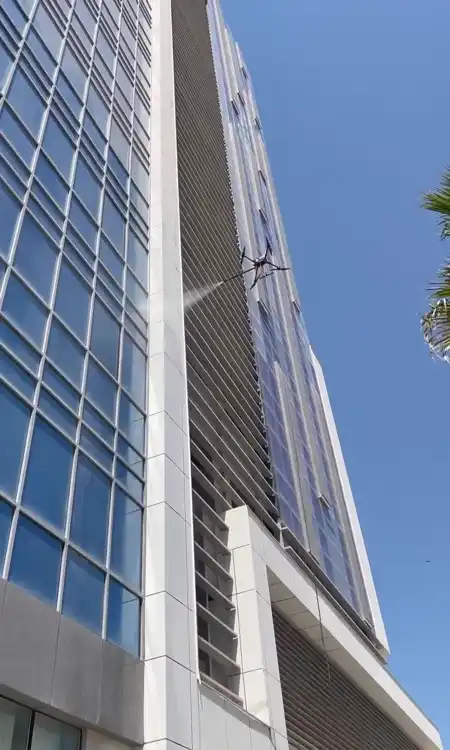 A tethered drone washing the glass facade of a tower, fed by a hose from the ground
